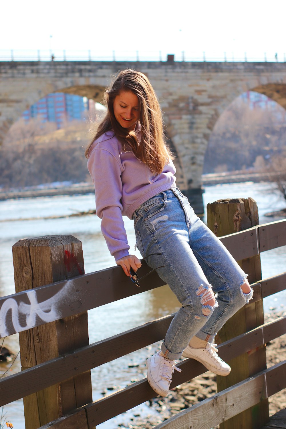 woman in pink long sleeve shirt and blue denim jeans sitting on brown wooden bench during