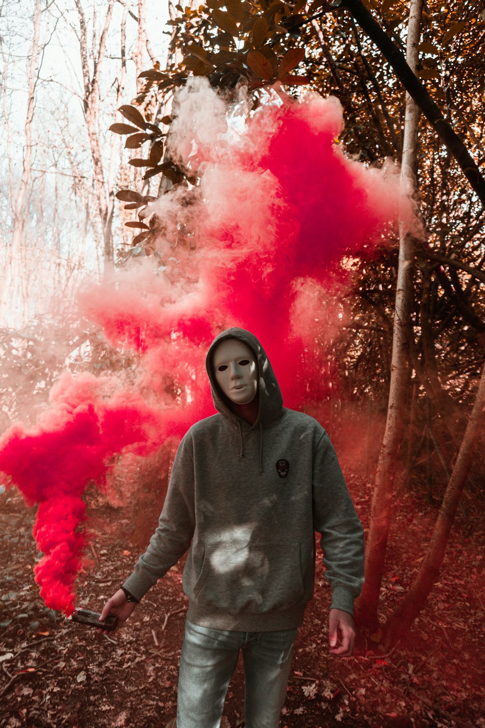 Mujer con sudadera con capucha gris de pie frente al humo rosa