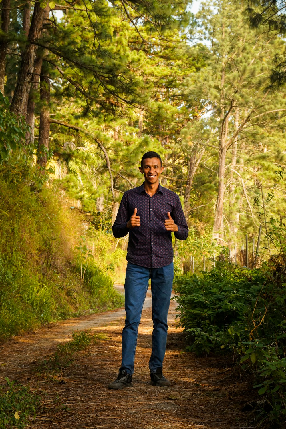 hombre en suéter negro de pie en camino de tierra entre árboles verdes durante el día