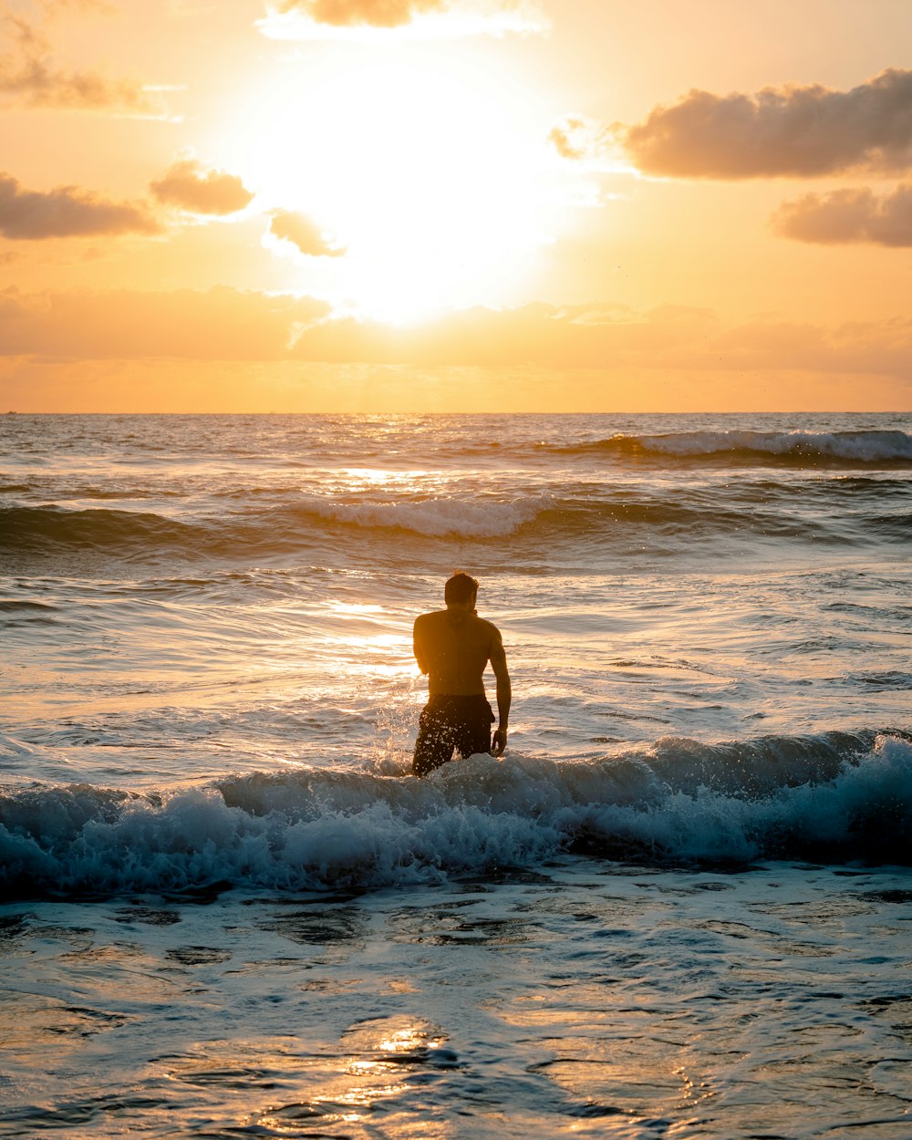 man in black shorts standing on sea waves during sunset