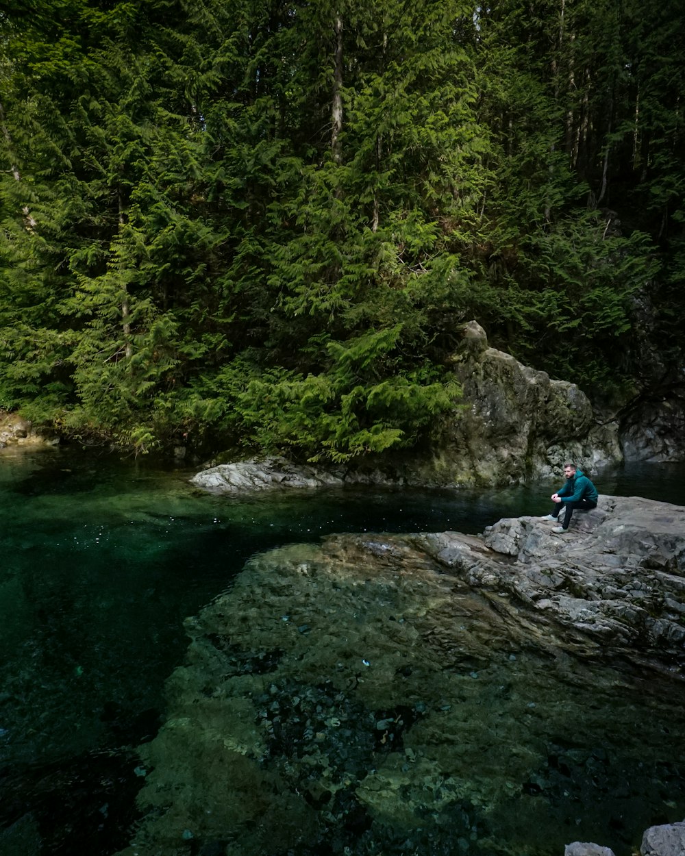 昼間、川の岩の上に座っている青いジャケットと青いデニムジーンズの男