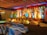 A beautifully decorated stage with vibrant floral arrangements and ornate backdrop. The stage is illuminated by colorful lights with red, yellow, and green hues. Chairs covered in white satin are arranged in rows facing the stage, and the ceiling is draped with multi-colored fabric, enhancing the festive atmosphere.