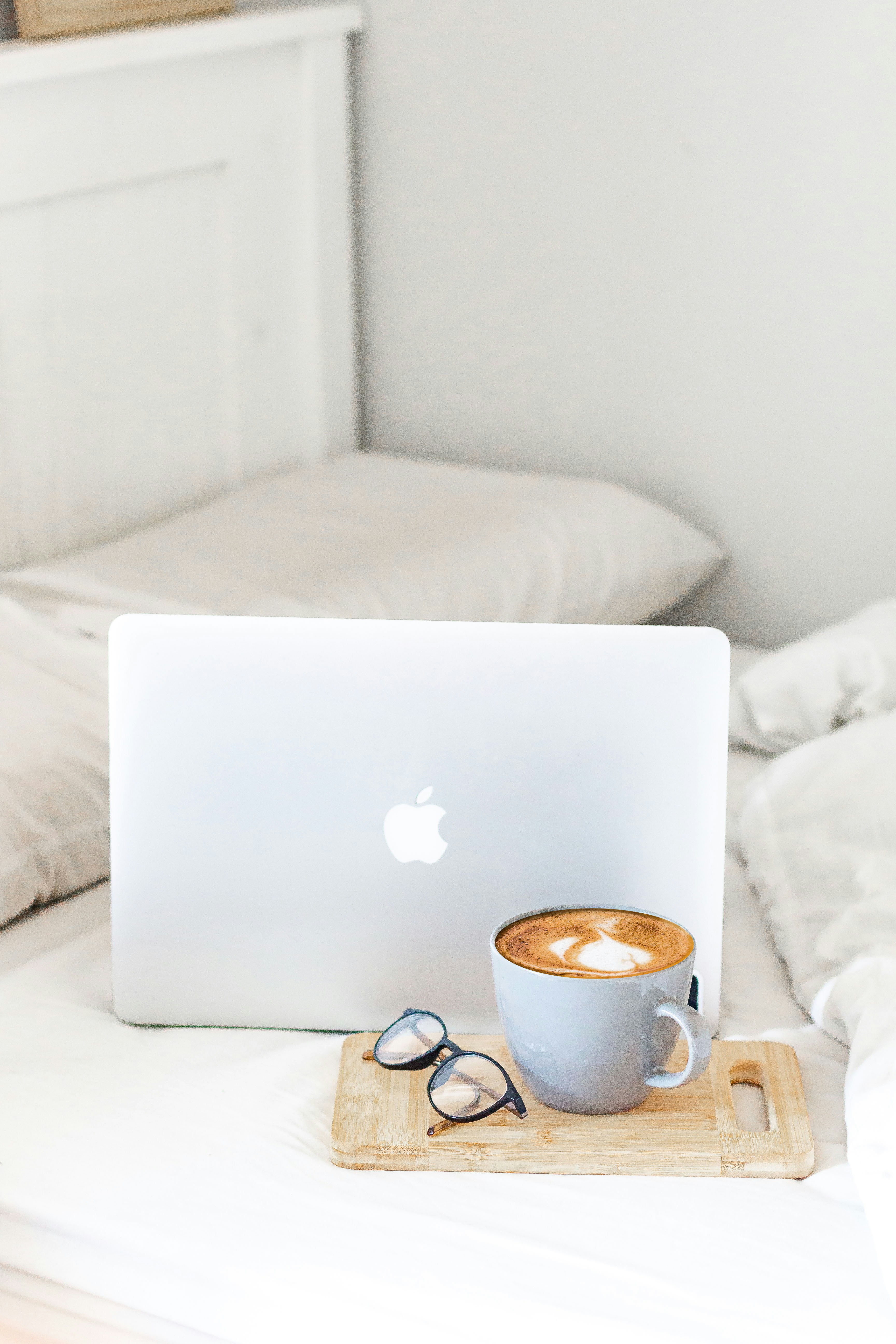 macbook air beside white ceramic mug on white bed