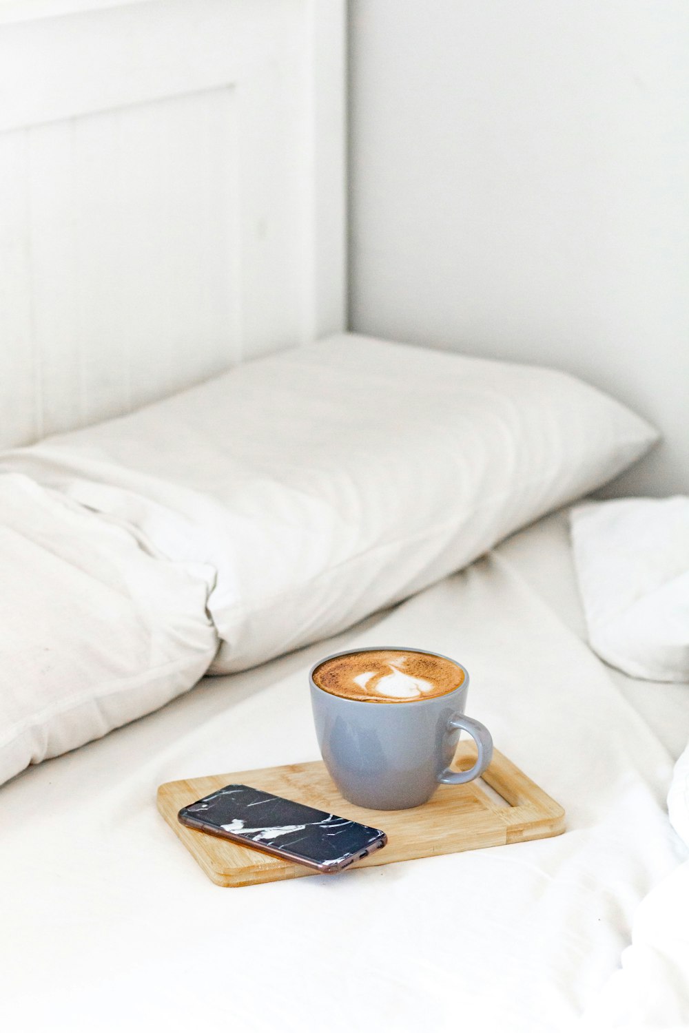 white ceramic mug on brown wooden tray beside black remote control