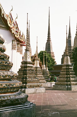 Intricate and colorful temple spires decorated with ornate patterns and surrounded by trees. The architecture includes tiered towers and traditional Thai elements, with attention to detail in the artwork.
