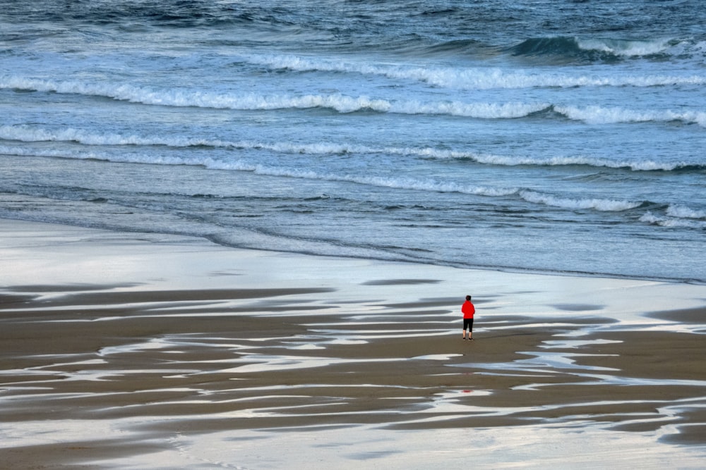 person in red shirt standing on seashore during daytime