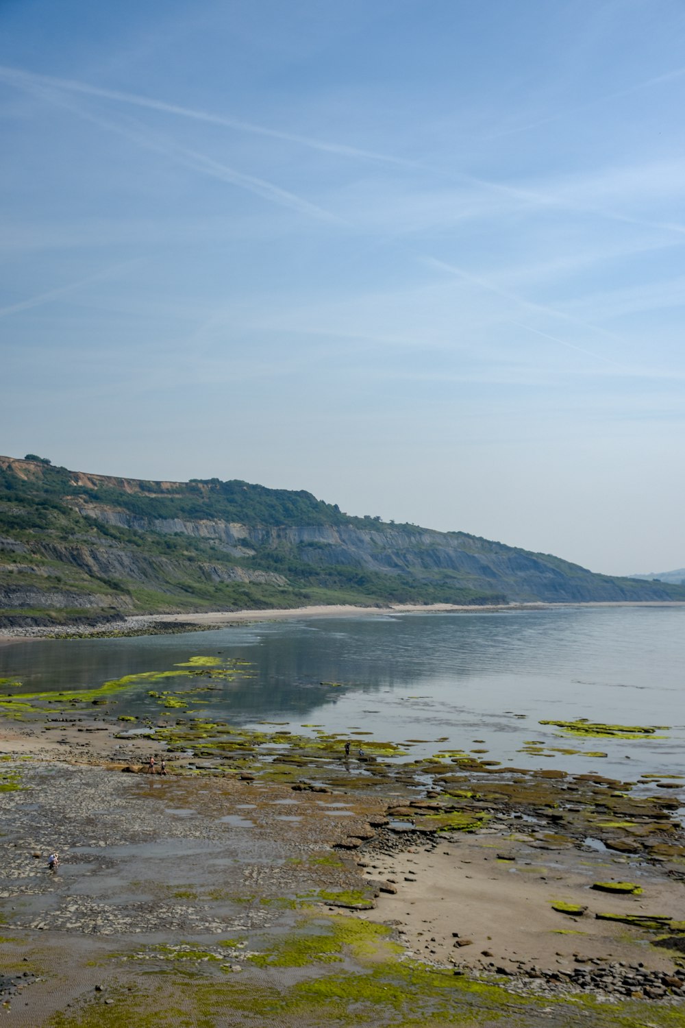 green and brown mountain beside body of water under blue sky during daytime