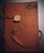 A brown leather notebook features an embossed design with scripted text and a postage stamp motif. It is wrapped with a leather cord that threads through the cover, adorned with a metallic key-shaped charm and a decorative plaque.