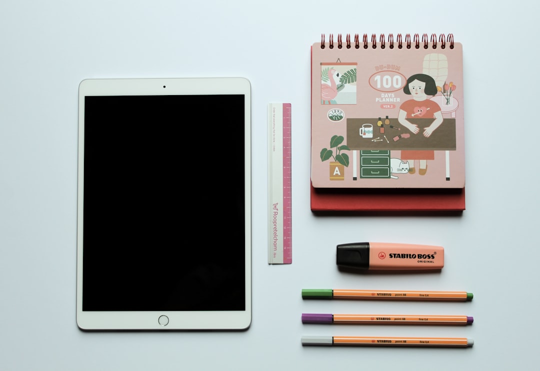 white ipad beside black and pink pen,