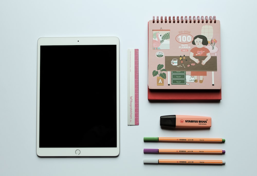 white ipad beside black and pink pen
