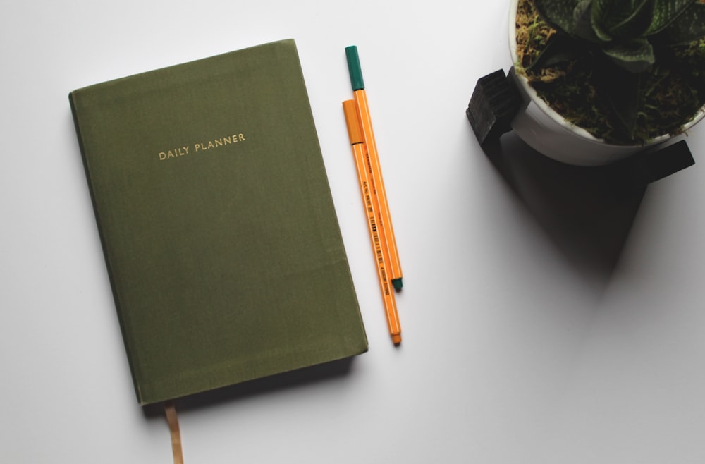 green book beside orange and white pen