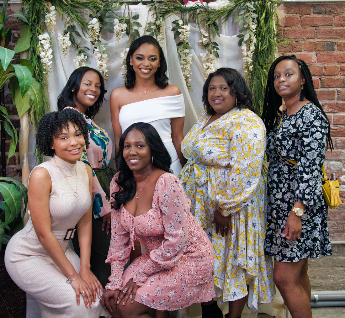 A bride-to-be smiling with her friends in front of a flower wall