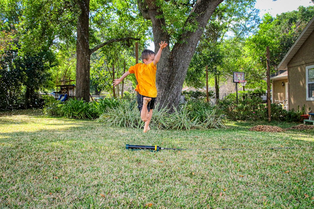 man in orange t-shirt and blue denim shorts standing on green grass field during daytime