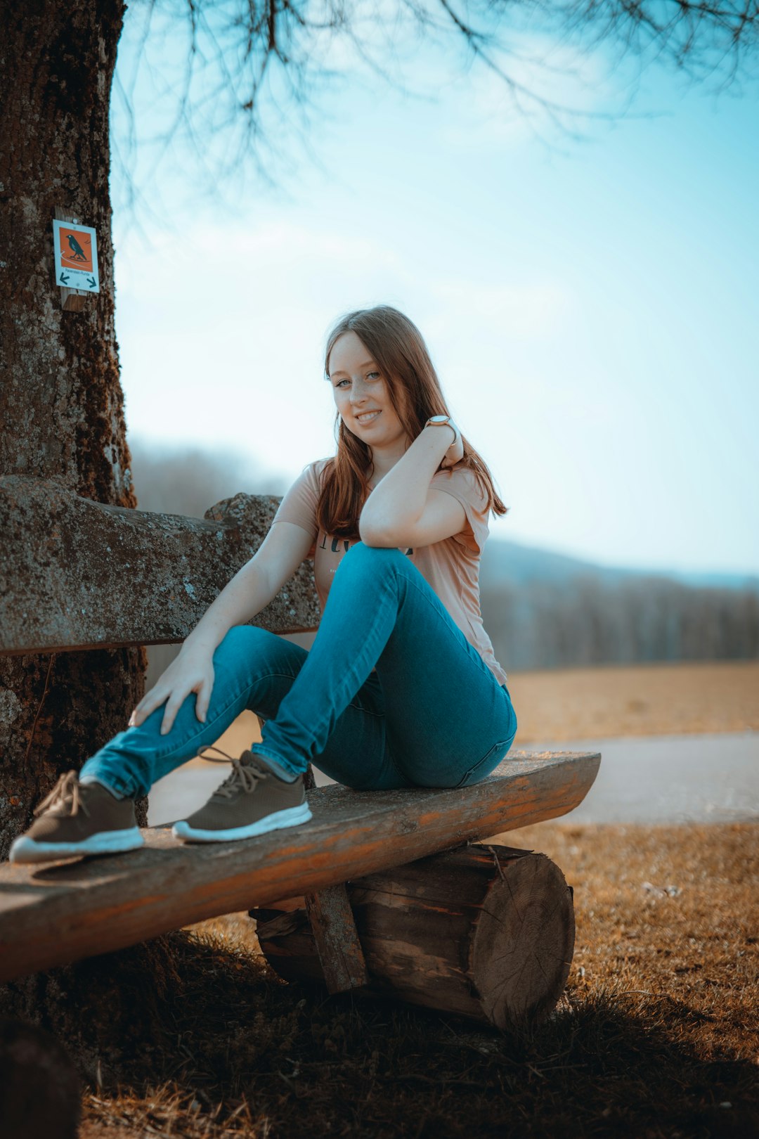woman in blue denim jeans sitting on brown wooden bench during daytime