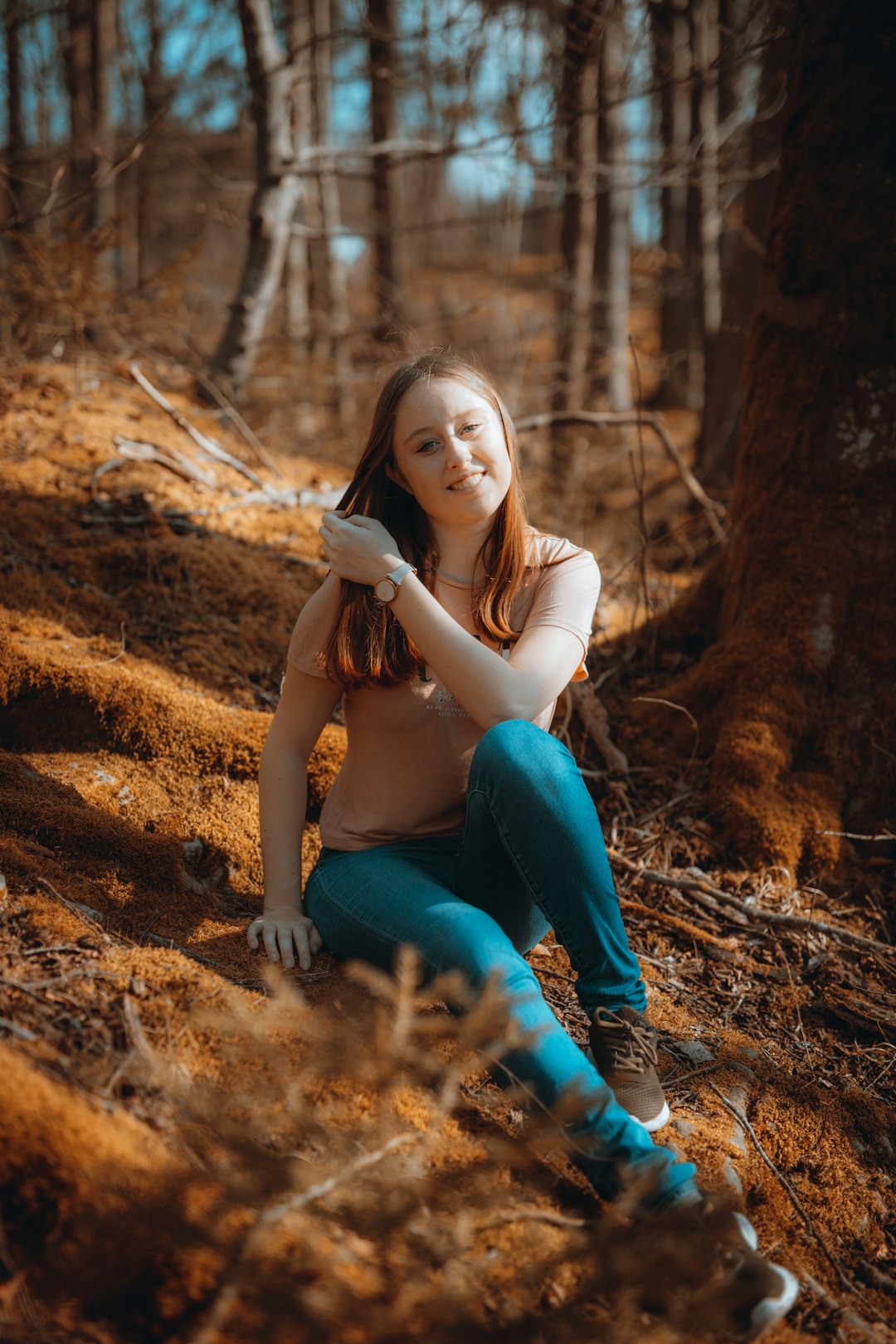 woman in blue denim jeans sitting on brown dried leaves during daytime