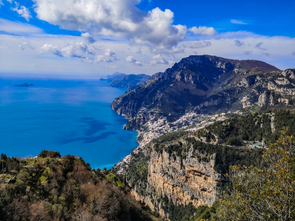 montanha verde e marrom ao lado do mar azul sob o céu azul durante o dia