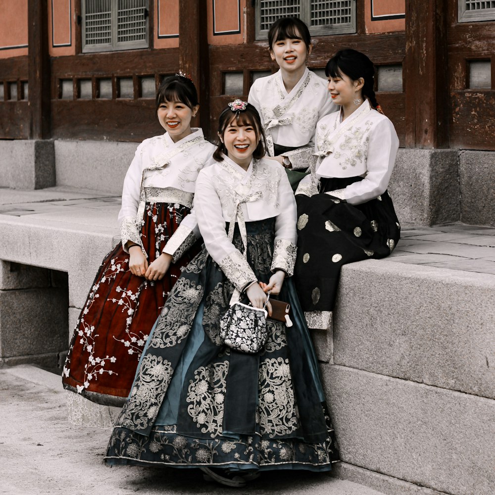 2 women in white and black long sleeve dress sitting on gray concrete bench during daytime