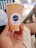 A hand holds a brown paper cup with a logo labeled 'Chiller'. The cup is eco-friendly and biodegradable, indicated by the text on it. The background is slightly blurred, showing part of a railing and sunlight casting shadows.