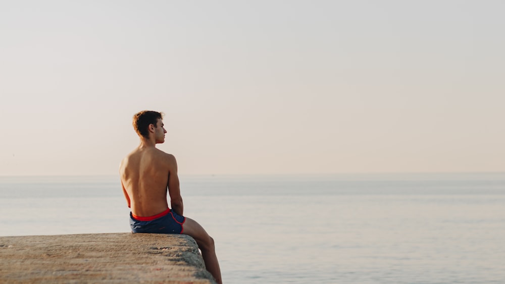 man in blue shorts sitting on rock