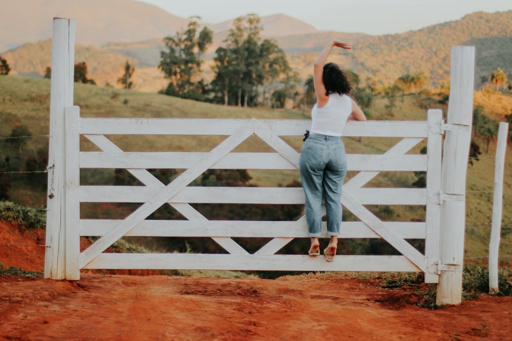 woman in white shirt and blue denim jeans standing on brown dirt road during daytime