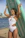 A smiling woman holding a paddleboard on a sunny beach with clear blue water behind her