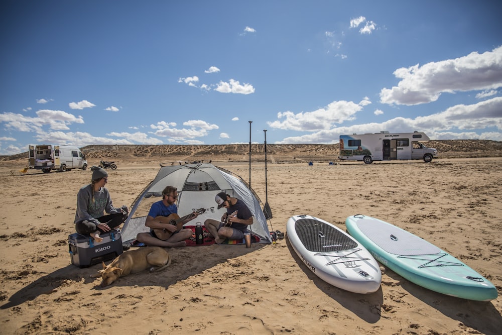 man in black t-shirt sitting on brown sand near white tent during daytime