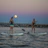Two practitioners playing soothing instruments on paddleboards during a sound journey at dusk.