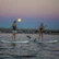 Two practitioners playing soothing instruments on paddleboards during a sound journey at dusk.