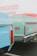 Vintage cars parked closely together with visible rear sections, showing distinct design details and emblem. Slightly blurred background with a hardware store sign.