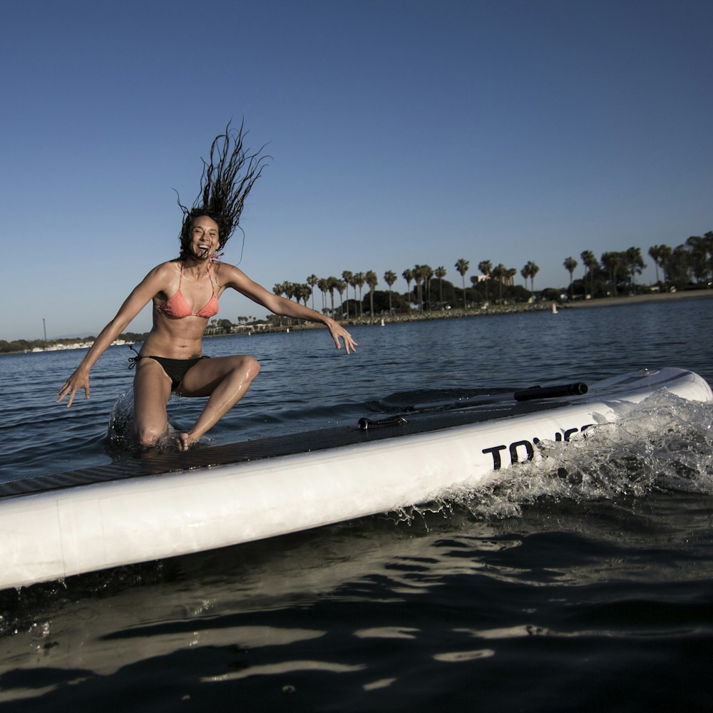 Mujer en bikini azul acostada en tabla de surf blanca en el mar durante el día