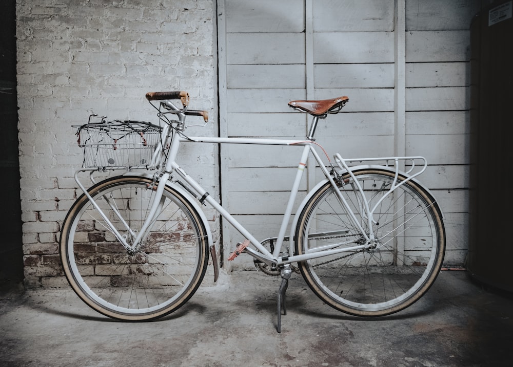 Bicicleta de carretera blanca y marrón apoyada en una pared de hormigón gris