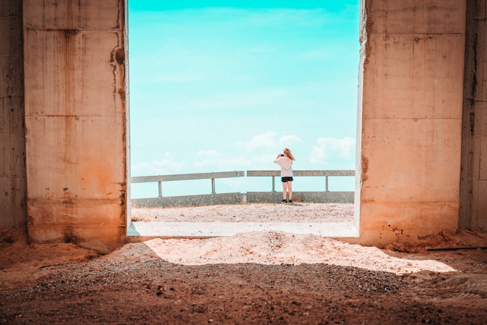 woman in white shirt and blue denim shorts standing on brown sand near sea during daytime