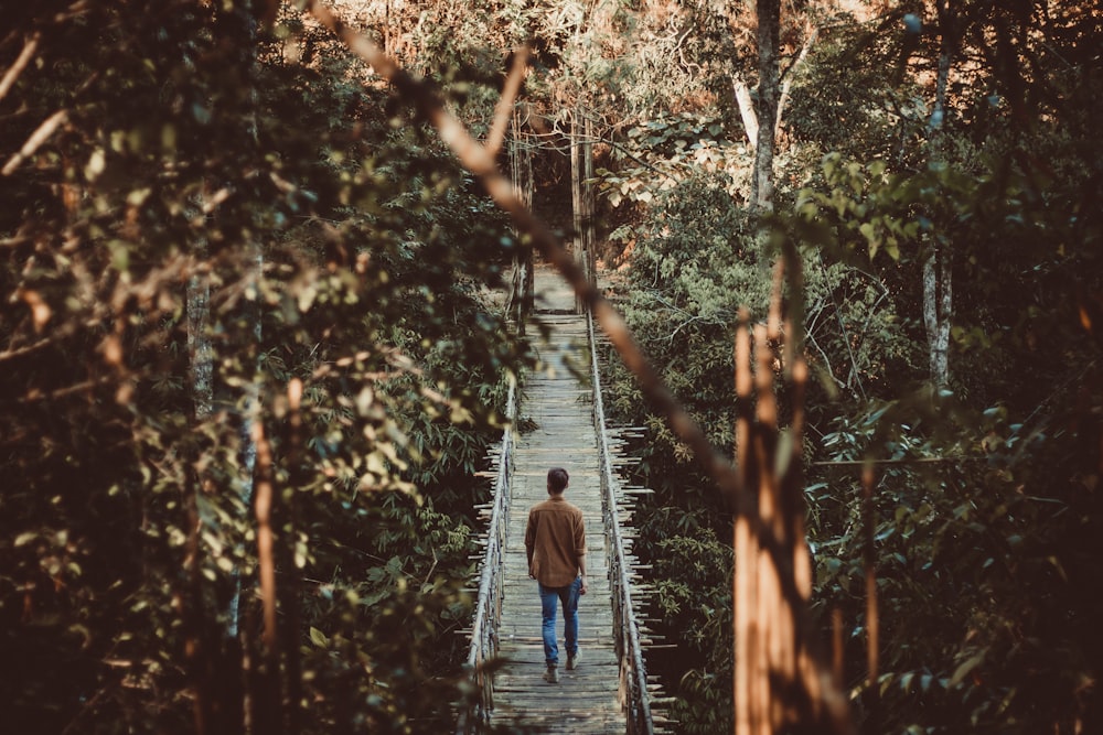 man in blue jacket walking on wooden bridge