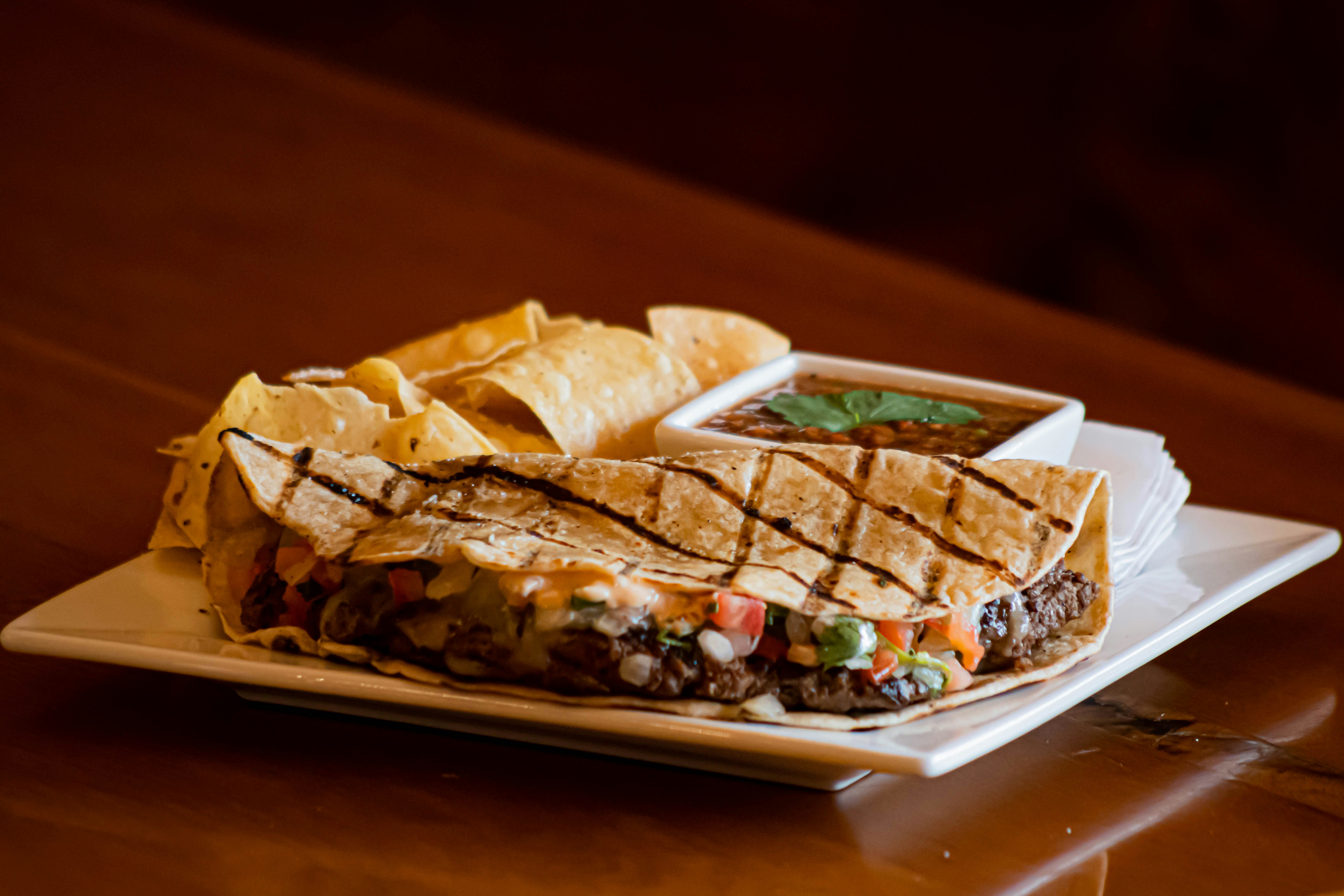 A golden-brown quesadilla cut in half, showing a filling of chicken, cheese, and colorful vegetables, served with a side of salsa