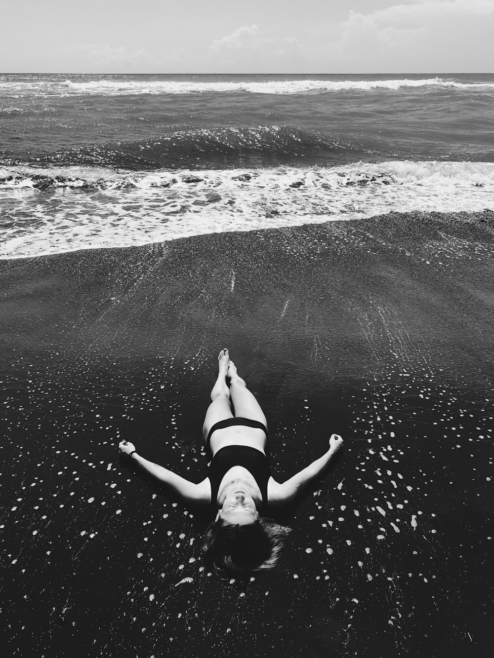 grayscale photo of woman lying on beach