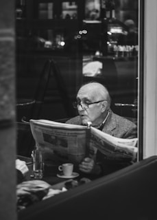 A person reading a newspaper in a cozy cafe with natural light streaming in.