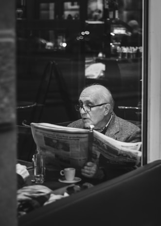 A person reading a newspaper in a cozy cafe with natural light streaming in.
