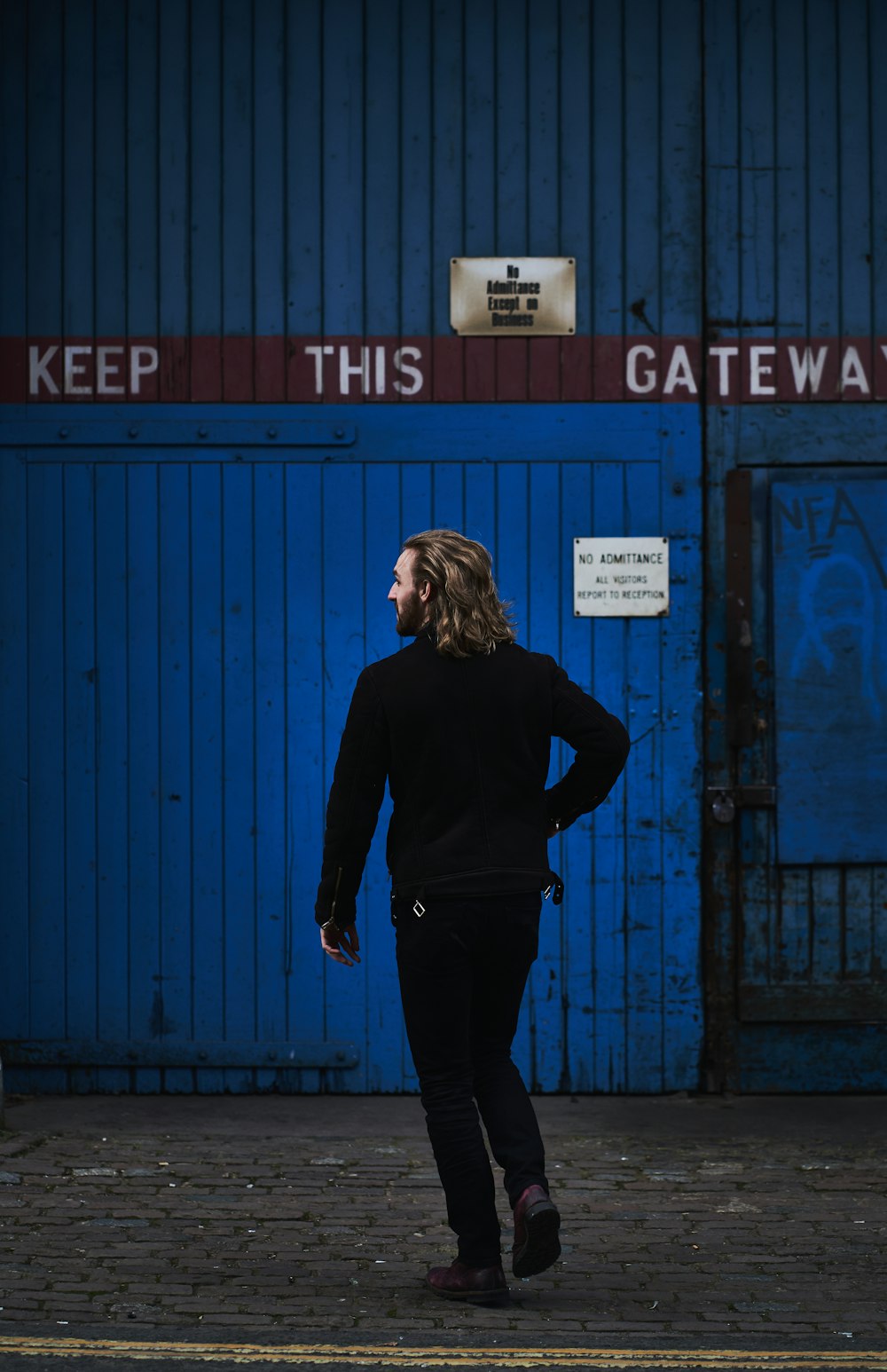 Mujer con camisa negra de manga larga y pantalones negros de pie frente a la puerta de madera azul