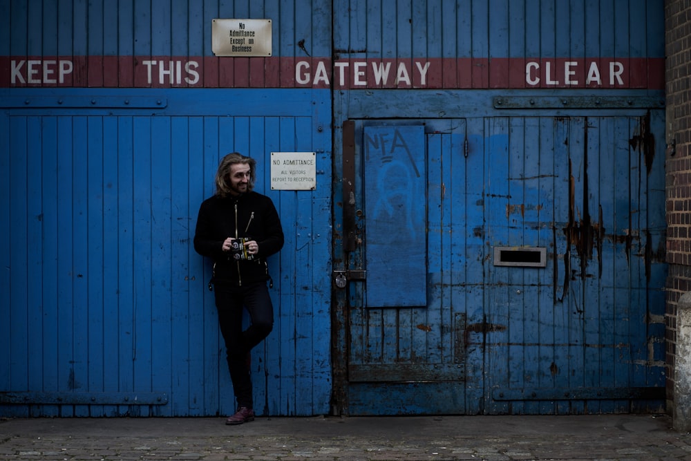 woman in black jacket standing beside blue wooden door