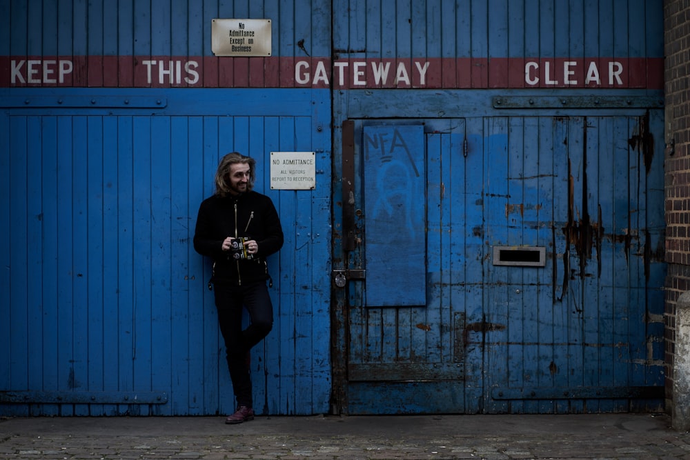 donna in giacca nera che si leva in piedi accanto alla porta di legno blu