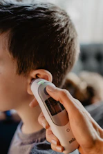 A smiling healthcare professional using a digital thermometer in a clinical setting.