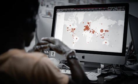A person is viewing a map with red data points on a computer monitor, likely indicating a geographical distribution. The image has a focus on technology and data analysis.