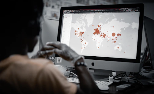 A person is viewing a map with red data points on a computer monitor, likely indicating a geographical distribution. The image has a focus on technology and data analysis.