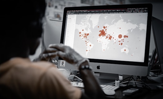 A person is viewing a map with red data points on a computer monitor, likely indicating a geographical distribution. The image has a focus on technology and data analysis.