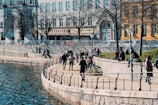 A scenic riverside promenade lined with trees and people enjoying a sunny day.