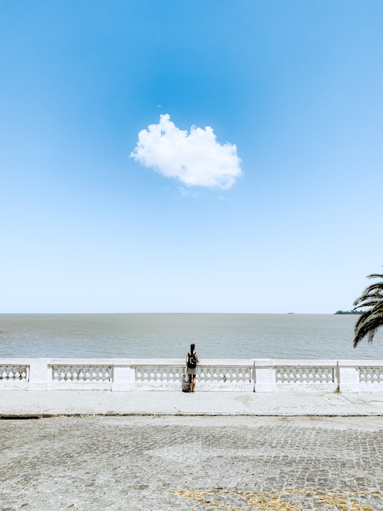 woman in black jacket and black pants standing on white wooden fence near body of water in Colonia Del Sacramento Departamento de Colonia Uruguay