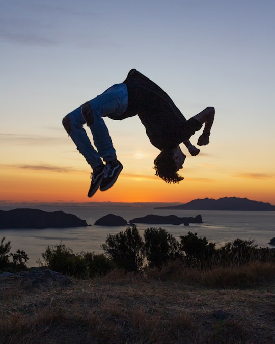 man in blue denim jeans jumping on brown field during sunset in Great Barrier Island New Zealand