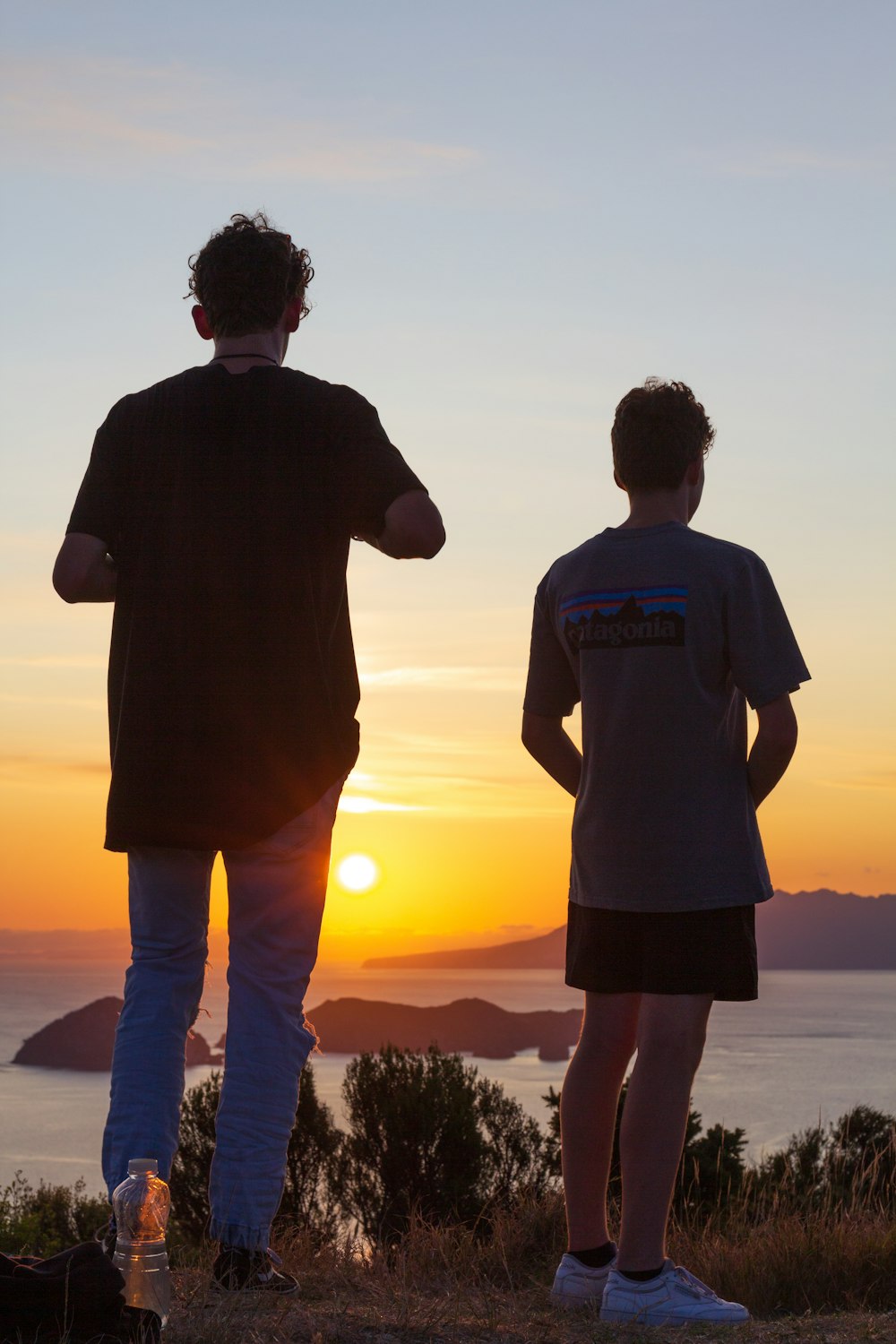 man in black crew neck t-shirt standing on seashore during sunset