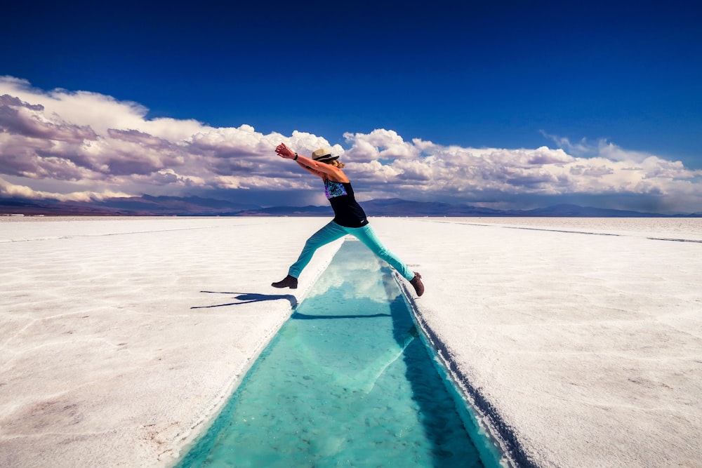 woman in black tank top and black shorts standing on blue surfboard on white sand beach