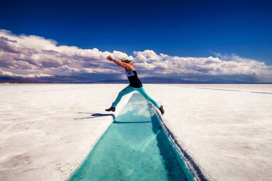 woman in black tank top and black shorts standing on blue surfboard on white sand beach in Jujuy Argentina